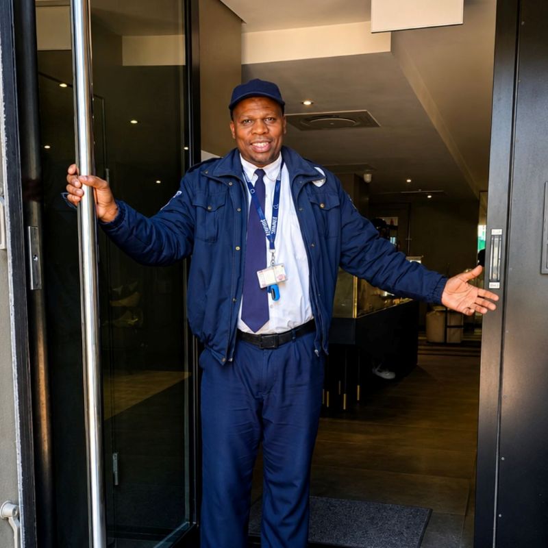 Smiling Empire officer holding open the entrance door of a residential building
